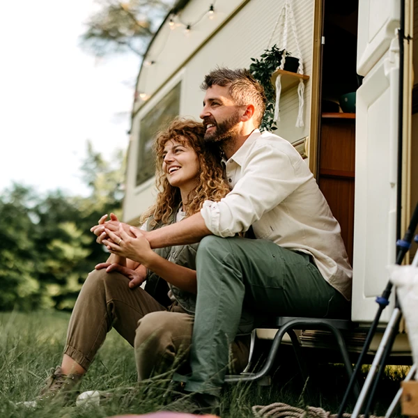 mid adult couple sitting on the steps of their camper, enjoying the outdoors